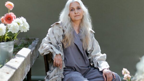 Senior woman in gray sitting indoors surrounded by flowers, creating a serene scene.