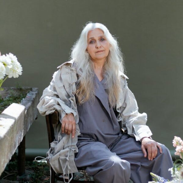 Senior woman in gray sitting indoors surrounded by flowers, creating a serene scene.