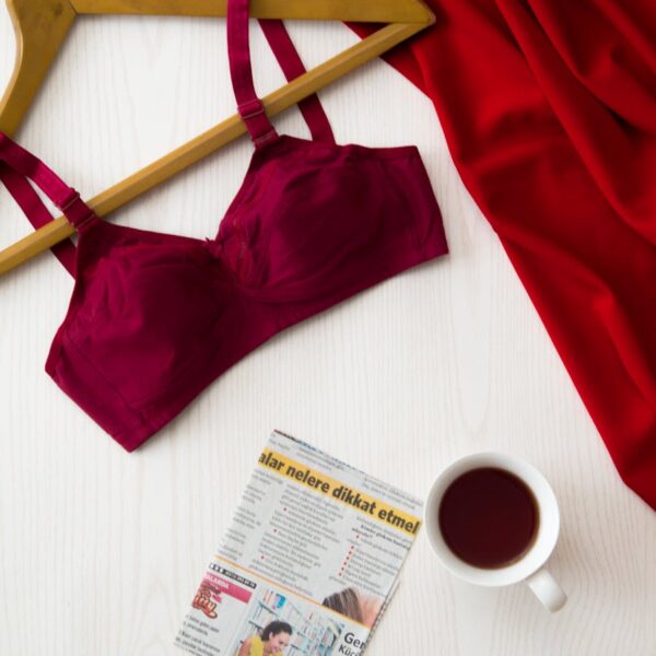 Red bra on hanger, cup of tea, newspaper, and red fabric on a white table for a modern and stylish look.