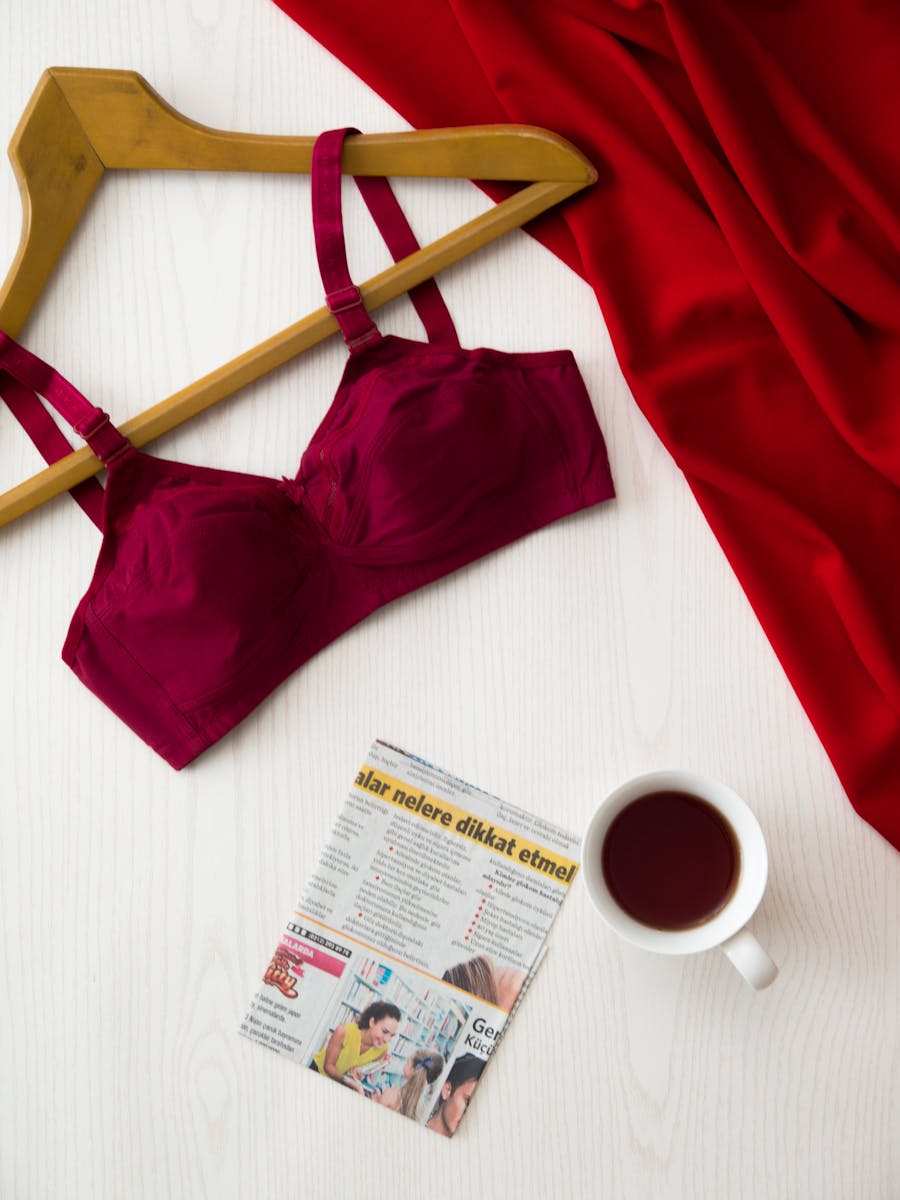 Red bra on hanger, cup of tea, newspaper, and red fabric on a white table for a modern and stylish look.