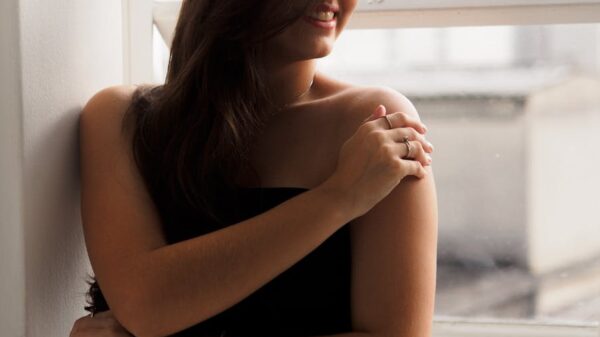 Elegant woman in a black dress standing by a window, smiling softly.