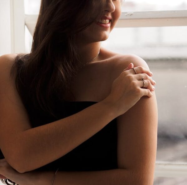 Elegant woman in a black dress standing by a window, smiling softly.