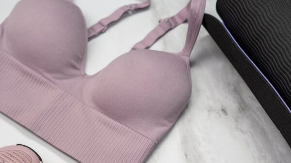 Pastel pink sports bra, sneakers, and yoga mat with earphones on marble.