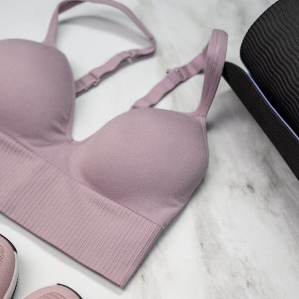 Pastel pink sports bra, sneakers, and yoga mat with earphones on marble.