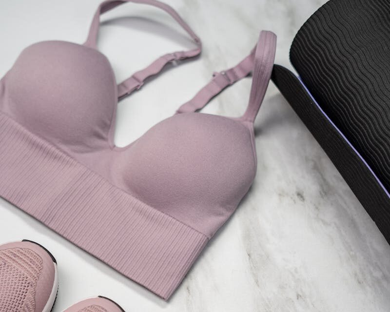 Pastel pink sports bra, sneakers, and yoga mat with earphones on marble.