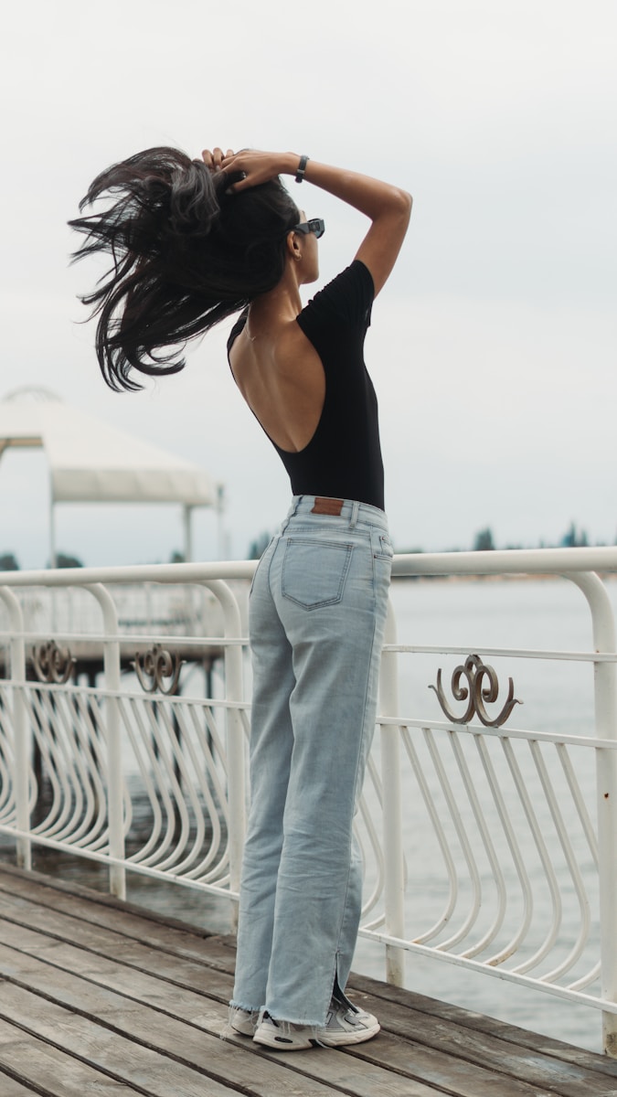 a woman standing on a pier with her hair blowing in the wind