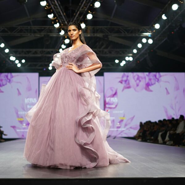Elegant model in lavender gown showcases high fashion on runway during Indian fashion week event.