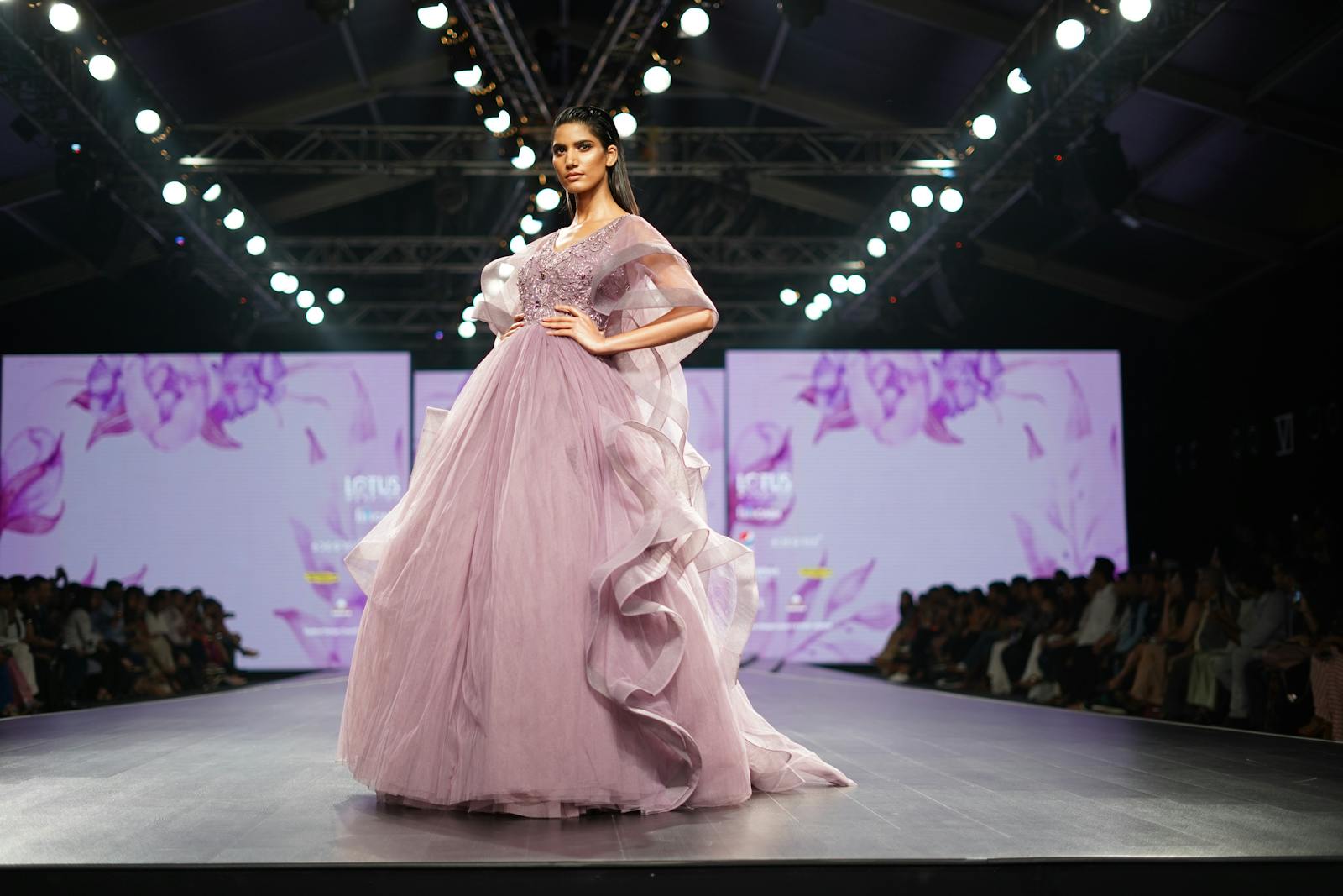 Elegant model in lavender gown showcases high fashion on runway during Indian fashion week event.