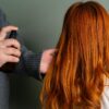 Close-up of hairdresser spraying hair product on long red hair.