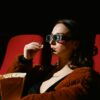 A woman enjoying a cinema experience wearing 3D glasses, holding popcorn.