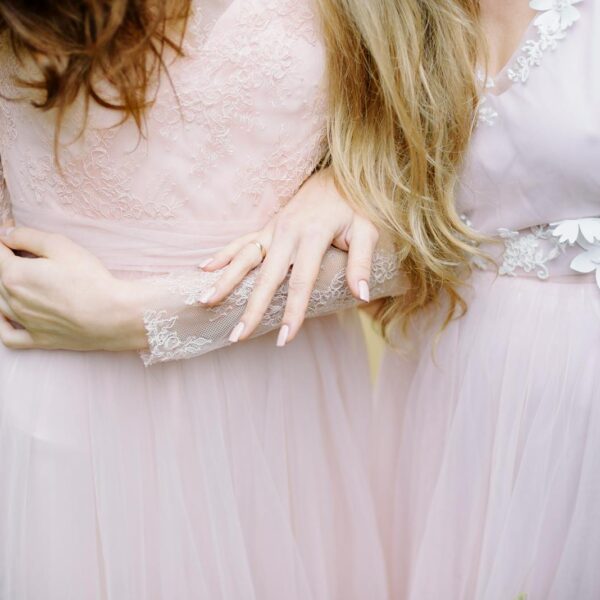 Close-up of bridesmaids in elegant, soft pink gowns showcasing intricate lace details outdoors.