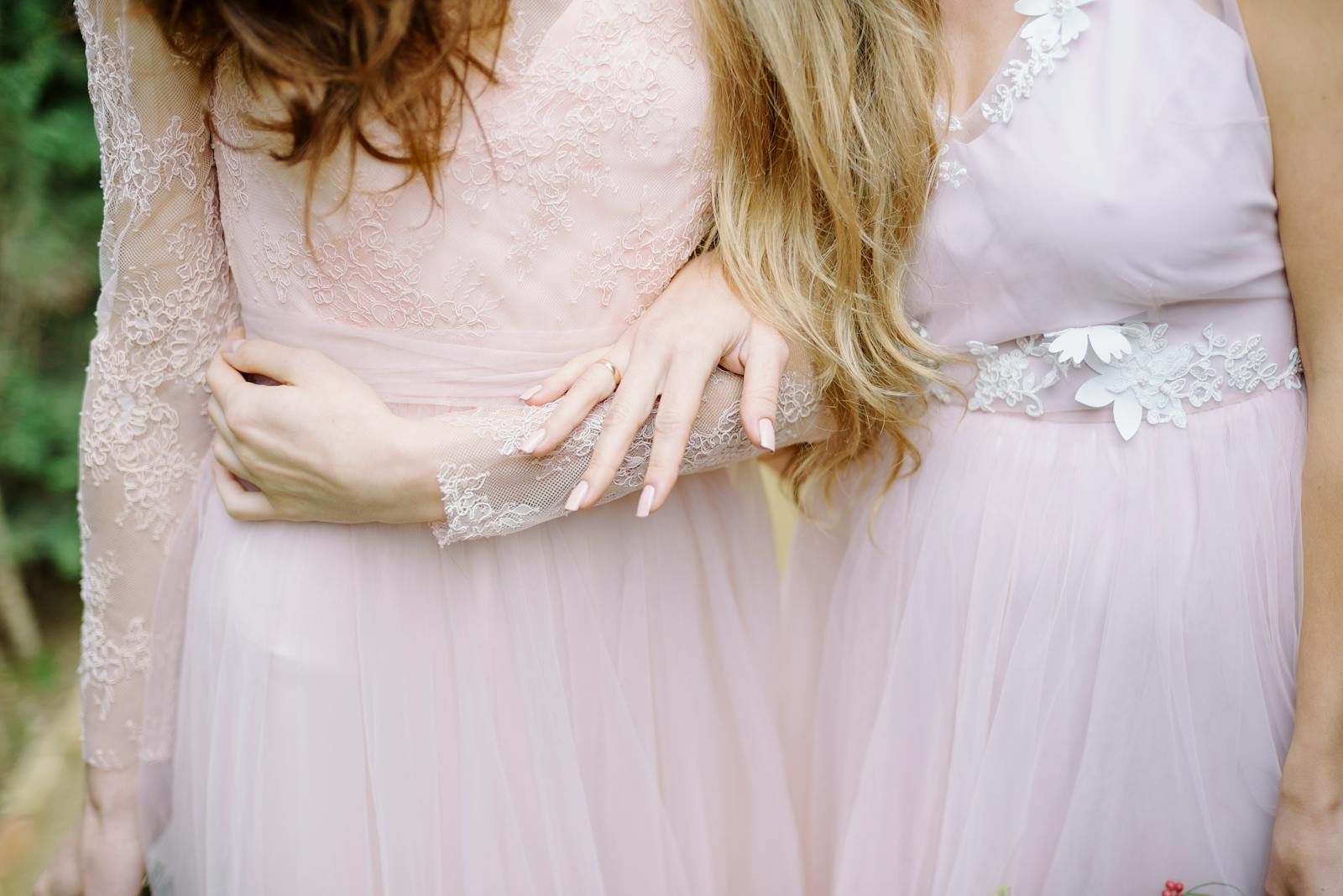 Close-up of bridesmaids in elegant, soft pink gowns showcasing intricate lace details outdoors.