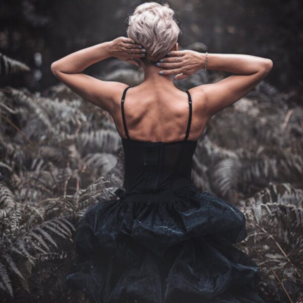Rear view of a woman in a black dress surrounded by a lush forest atmosphere.