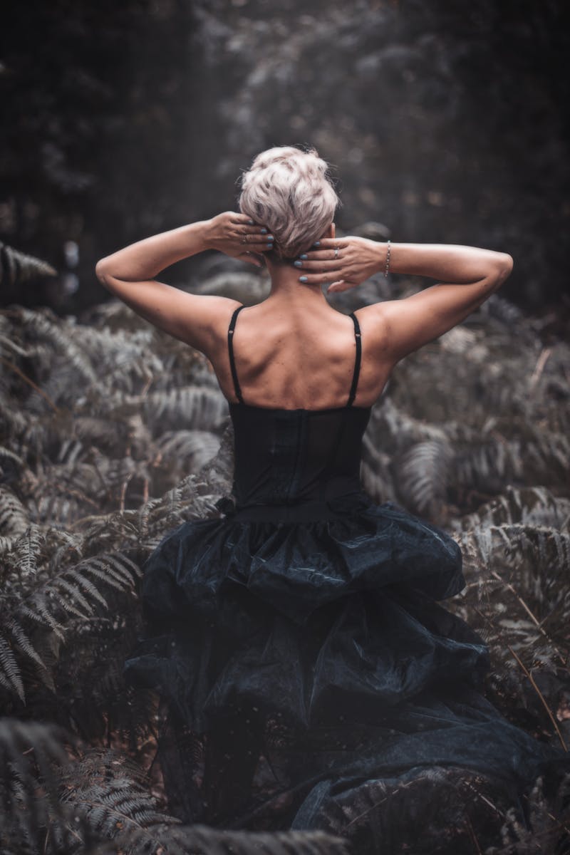 Rear view of a woman in a black dress surrounded by a lush forest atmosphere.