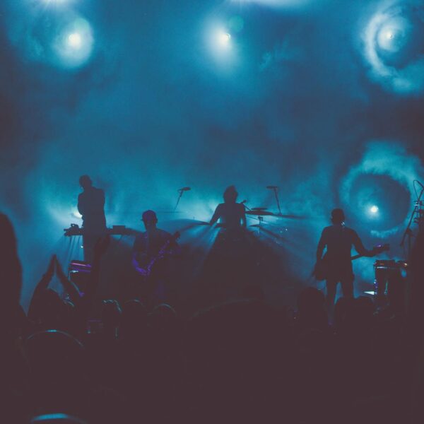 Silhouetted band performing on a smoke-filled stage with dramatic lighting.