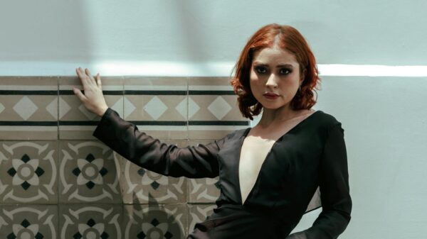 Woman in a chic black dress poses against a patterned wall, exuding elegance.