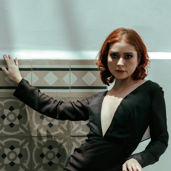 Woman in a chic black dress poses against a patterned wall, exuding elegance.