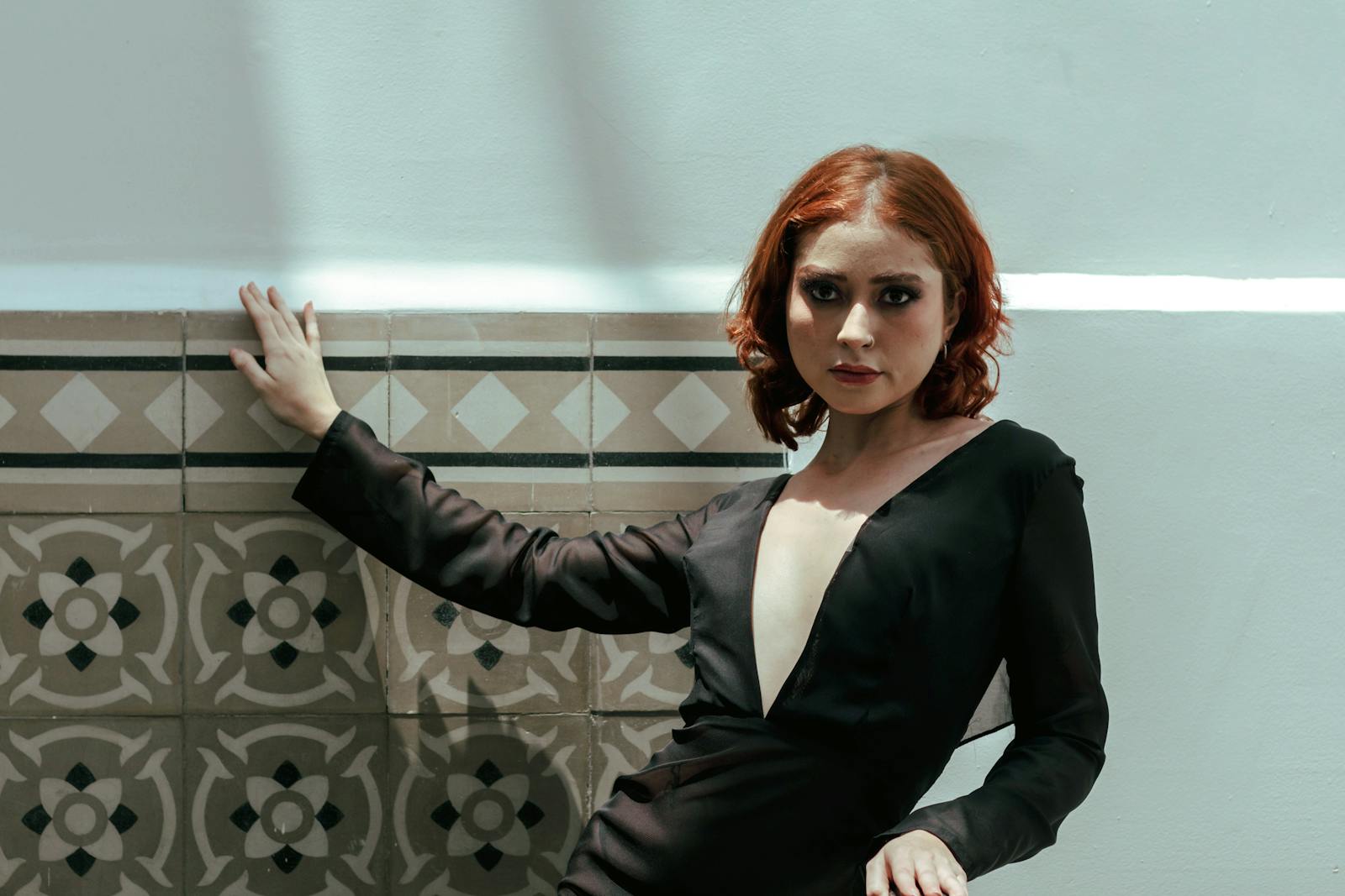 Woman in a chic black dress poses against a patterned wall, exuding elegance.