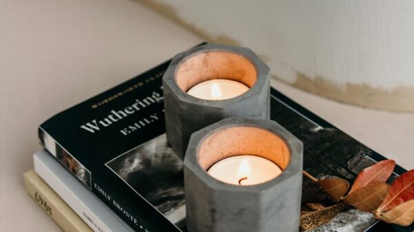 Composition of burning tealights in candleholders placed on stacked books on white surface