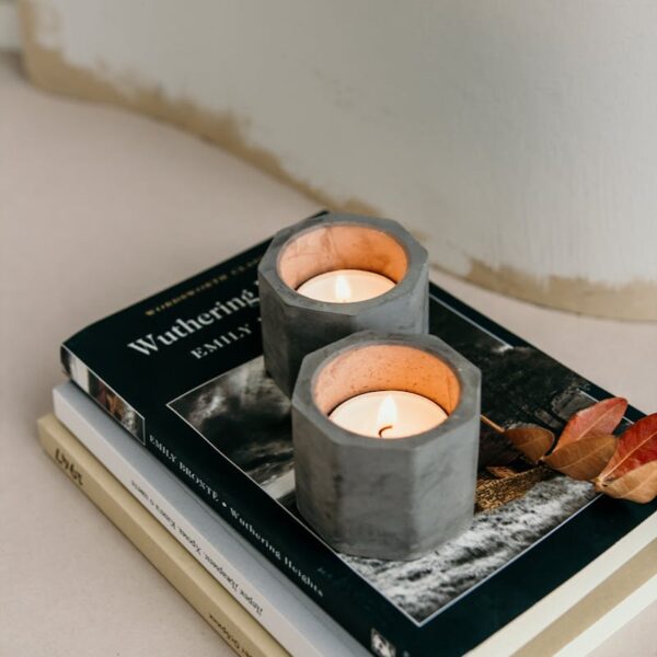 Composition of burning tealights in candleholders placed on stacked books on white surface