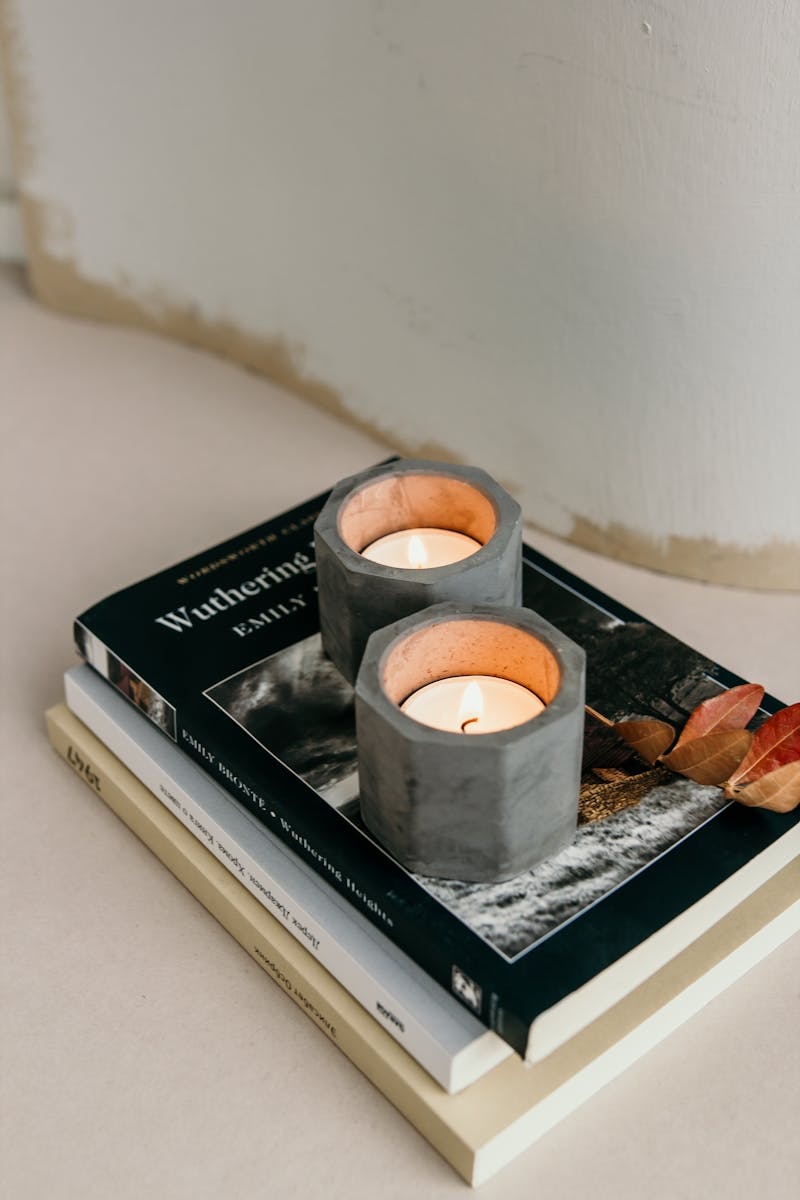 Composition of burning tealights in candleholders placed on stacked books on white surface