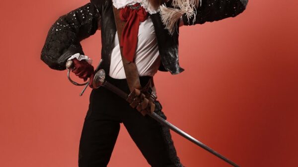 Portrait of a woman in pirate costume joyfully posing with a sword against a red studio background.