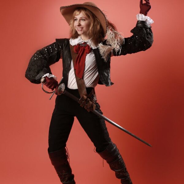 Portrait of a woman in pirate costume joyfully posing with a sword against a red studio background.