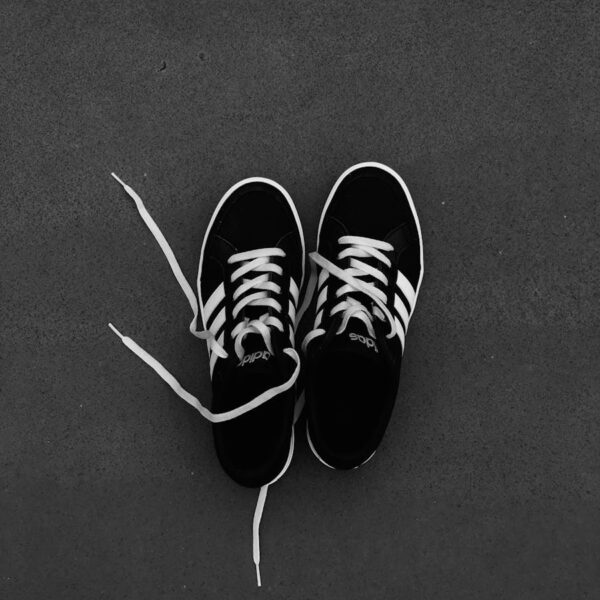 A close-up shot of black sneakers with white laces on a dark surface.