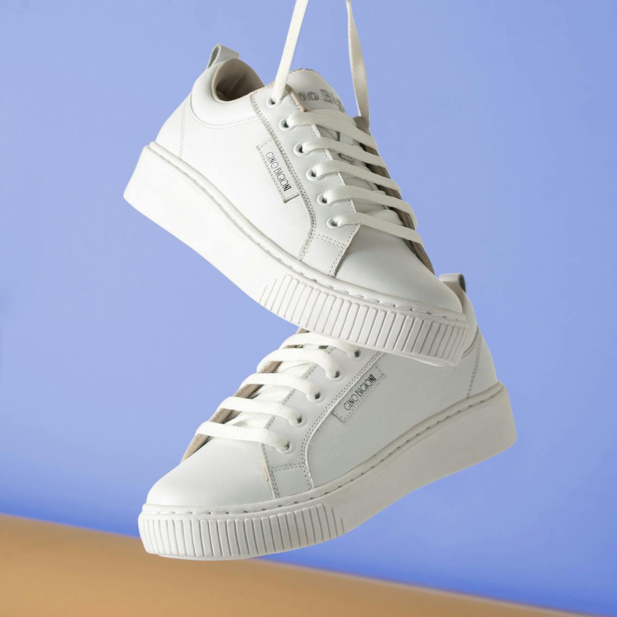 Minimalist white sneakers hanging against a soft blue backdrop for fashion product focus.
