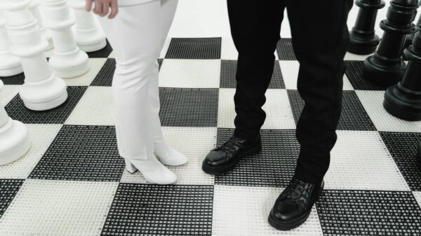 Giant chess pieces on a checkered board with two people in contrasting outfits, symbolizing strategic confrontation.