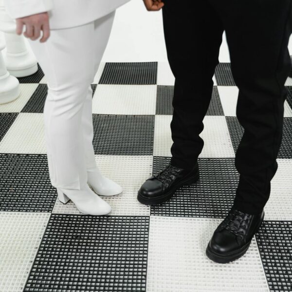 Giant chess pieces on a checkered board with two people in contrasting outfits, symbolizing strategic confrontation.