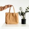 Stylish minimalist canvas tote bag held beside a potted green plant.