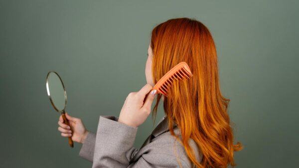 Red-haired woman using a comb while holding a mirror, focusing on hair care and beauty.