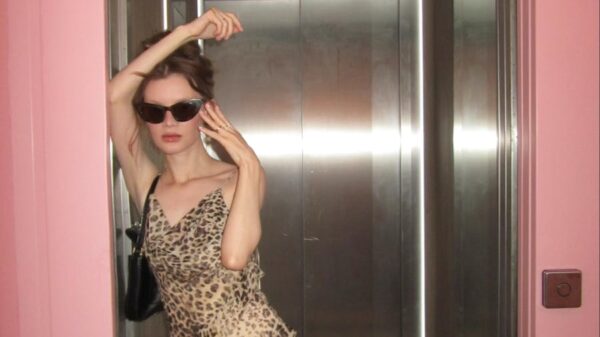 Fashionable woman in leopard print dress posing in elevator with pink walls.