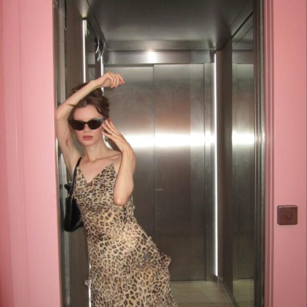 Fashionable woman in leopard print dress posing in elevator with pink walls.