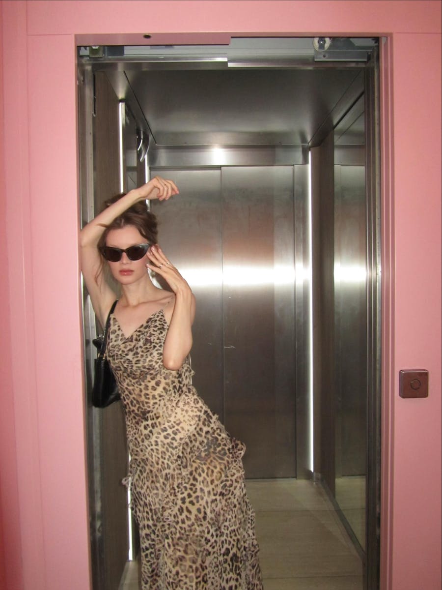 Fashionable woman in leopard print dress posing in elevator with pink walls.