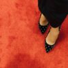 Black high heel shoes with studded design on vibrant red carpet. Fashion statement.