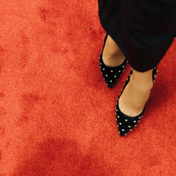 Black high heel shoes with studded design on vibrant red carpet. Fashion statement.
