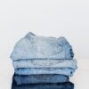Pile of denim pants of different shades of blue placed on white shelf