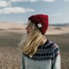 Side view of young female in casual warm sweater and red knitted hat standing in dry desert