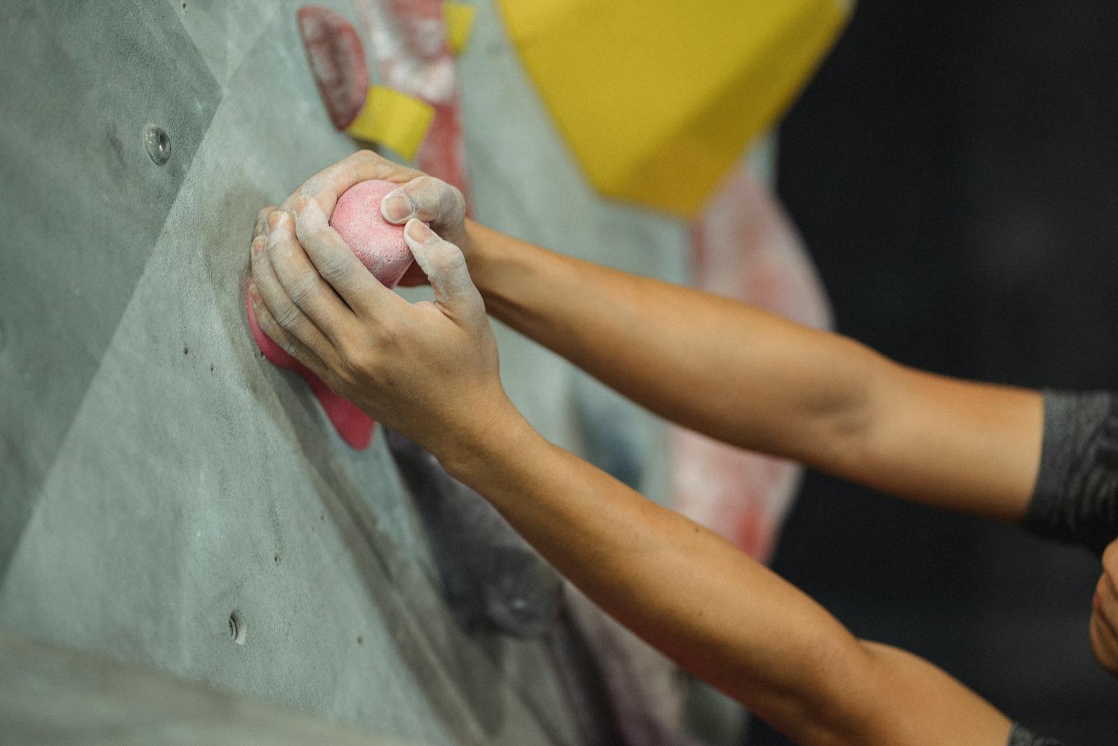 From above of crop male climber putting hands in talcum powder on pink climbing hold during training in gym