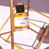 Close-up of perfume bottle elegantly displayed in a gold geometric frame with warm lighting.