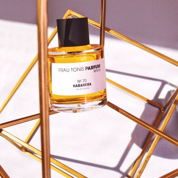 Close-up of perfume bottle elegantly displayed in a gold geometric frame with warm lighting.