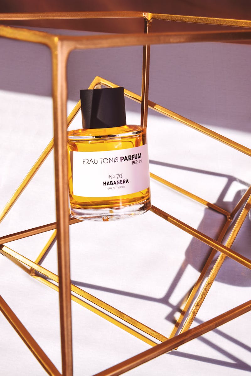 Close-up of perfume bottle elegantly displayed in a gold geometric frame with warm lighting.