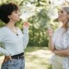 Two women smoking and conversing in a lush green outdoor setting, enjoying a moment of relaxation.