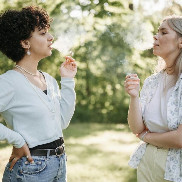 Two women smoking and conversing in a lush green outdoor setting, enjoying a moment of relaxation.