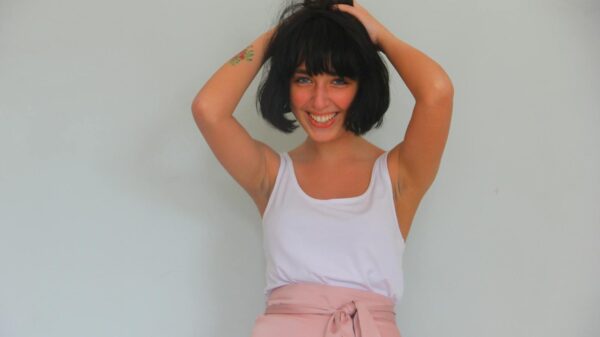 Smiling woman in white tank top and pink skirt posing playfully indoors.
