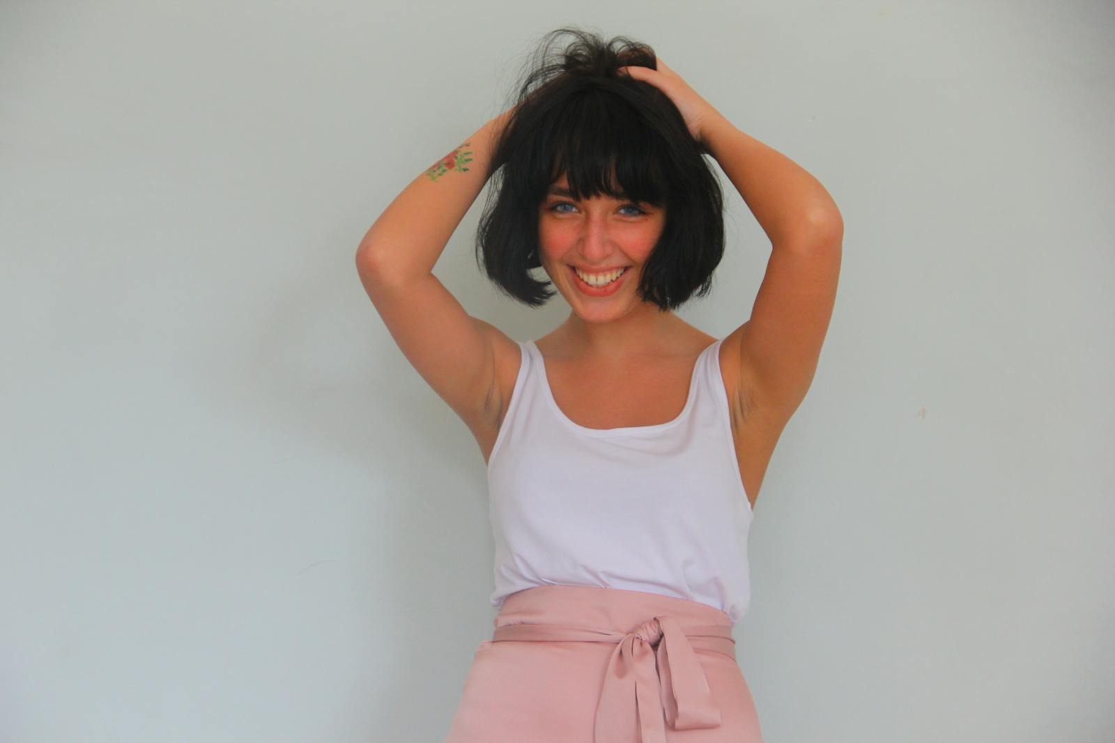 Smiling woman in white tank top and pink skirt posing playfully indoors.