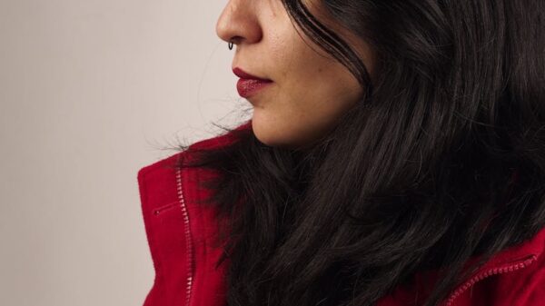 Side profile of a woman with dark hair in a red jacket, studio setting.