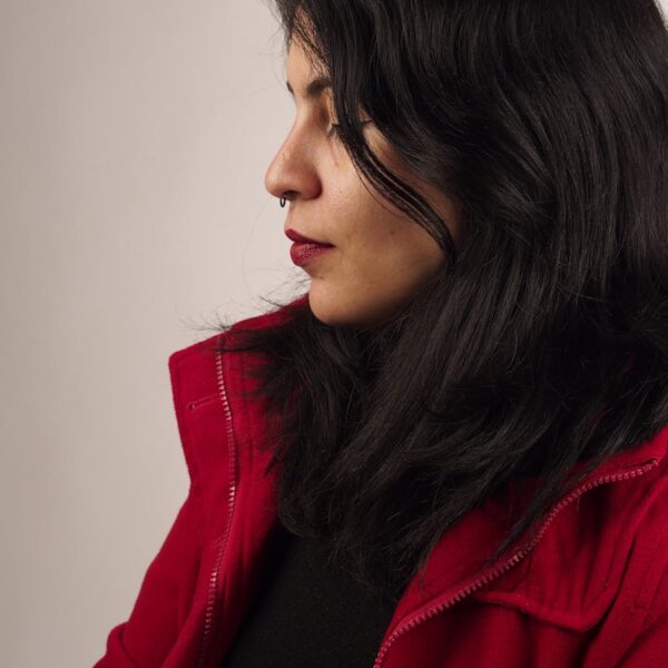Side profile of a woman with dark hair in a red jacket, studio setting.